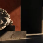 Classical marble head resting on its side on a stone plinth in a dark gallery