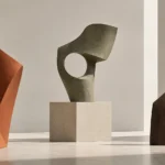 Three abstract sculptures in terracotta, sage stone and bronze with open holes in a gallery